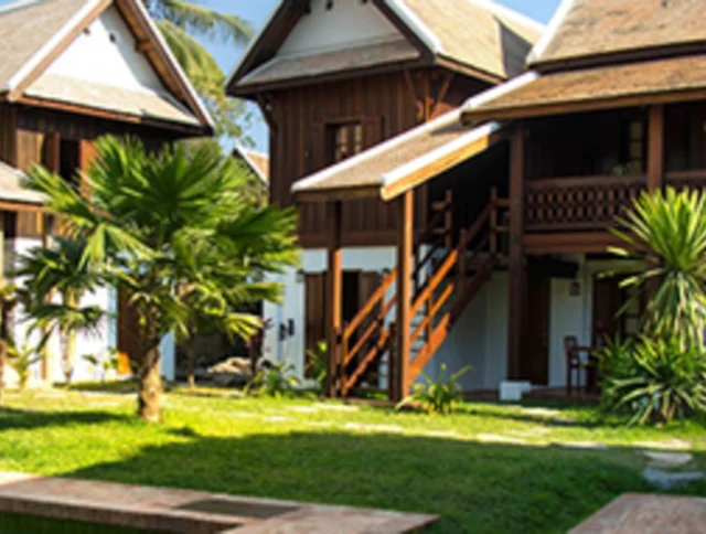 Traditional wooden houses with steep roofs surround a small grassy courtyard, featuring tropical plants and a path leading to the entrance.
