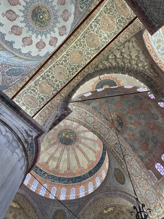 Ornate interior arches and domes of a decorated mosque ceiling, featuring intricate patterns and geometric designs in muted colors.