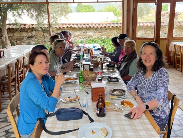A group of people dining at a restaurant with wooden decor. Plates with food and drinks are on the table. Several people are smiling at the camera.