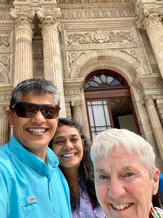 Three people smiling in front of an ornate historic building with tall columns and intricate carvings.