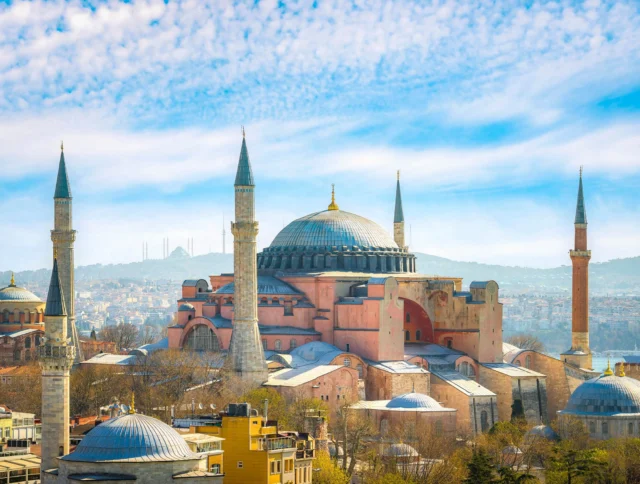 A view of Hagia Sophia in Istanbul, featuring its large dome and four minarets under a partly cloudy sky.