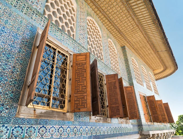 Building facade with intricate blue mosaic tiles and wooden windows open outward under a patterned roof.