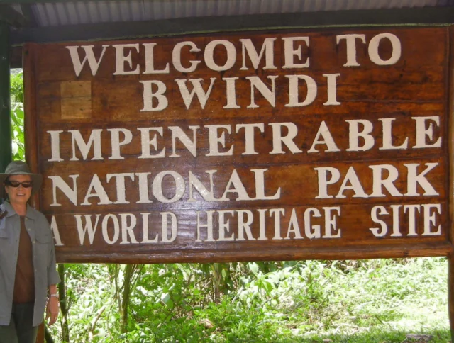 A person stands next to a sign reading, "Welcome to Bwindi Impenetrable National Park, A World Heritage Site.
