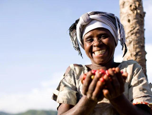 Smiling woman holding a handful of ripe, red berries in an outdoor setting.