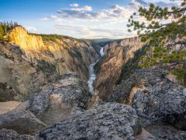 View of a rocky canyon with a river flowing through it, surrounded by cliffs and trees under a partly cloudy sky.